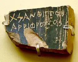 A shard of black pottery, worn with a name carved in Greek letters