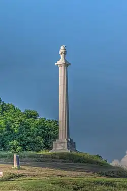 Photo shows a tall, white column, with a torch at the top.