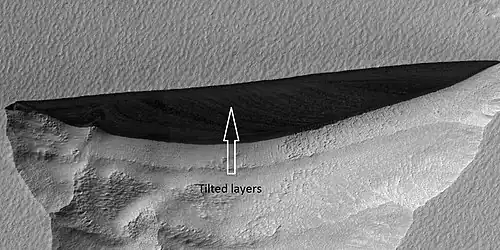 Close view of wall of triangular depression, as seen by HiRISE layers are visible in the wall. These layers contain ice. The lower layers are tilted, while layers near the surface are more or less horizontal. Such an arrangement of layers is called an "angular unconformity".[245]