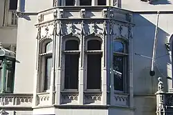 Detail of a three-sided bay window to the left of the entrance. The bay window is divided into two window panes at the center and one smaller pane on either side.