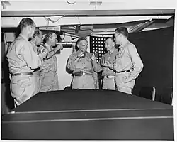 Black and white photograph of six men in khakis standing around a table raising their glasses