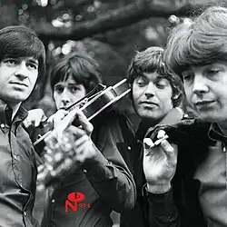 A closeup black-and-white photo of the four band members with a tree in the background.