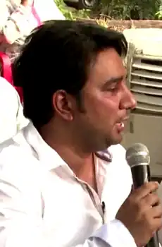 Ahmed Khan wearing a white shirt and holding a microphone, looking left of camera