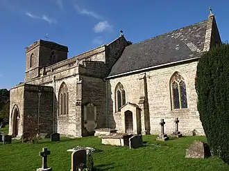 Stone building with square tower to left hand end. Foreground shows gravestones in grass area.