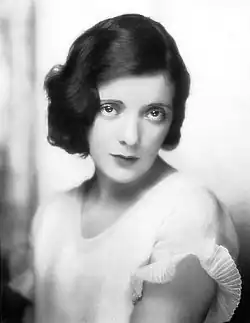Black and white portrait photograph of a young woman with dark hair and dark eyes, wearing what appears to be a light-colored dress or blouse