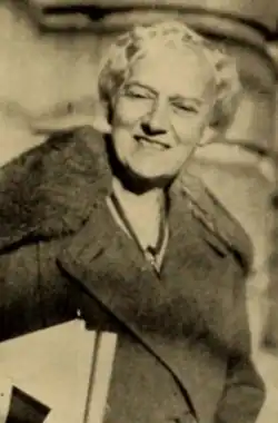 A smiling older white woman with white hair in a set style, wearing a coat with a fur collar
