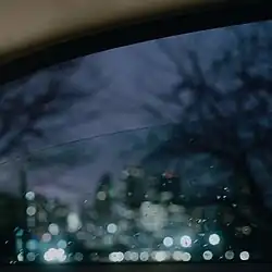 A blurred photo of skyscrapers taken from inside a car window with rain on it