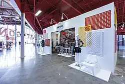 A white, roofless structure, similar to a large cubicle, containing a clothing store called "Pletora".