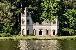 An off-white Gothic façade with arched windows on the far side of a lake