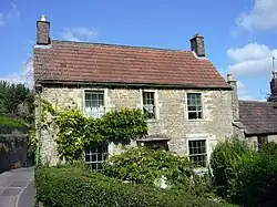 Two storey stone house with red roof. Partially obscured by vegetation