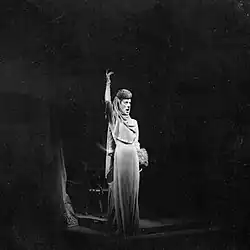 white woman in plain evening dress singing and gesticulating exaggeratedly