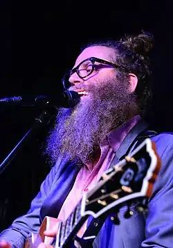 close-up of Ben Caplan playing an acoustic guitar and singing into a microphone onstage