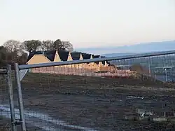 A row of newly built yellow houses seen at a slightly off angle through a construction site fence.
