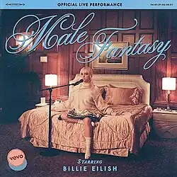 Cover art for the official live performance of "Male Fantasy": Billie Eilish on a hotel room bed, with a microphone stand next to her. Above her is the song title, written in blue and in a cursive font.