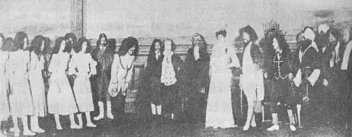 A black-and-white image of a group of people at a party; these include several dressed in long robes, as well as individuals in diverse formal garb.