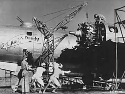 A black and white photograph of multiple men repairing the engine of a plane