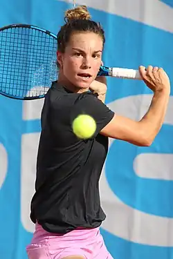 Headshot of Loïs Boisson preparing to hit a tennisball. She is a young, white woman with dark hair in a bun wearing a black jersey and pink shorts.