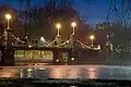 Boston Public Garden Foot Bridge at night, 2007. The bridge is illuminated by lampposts, and several people are standing on it.