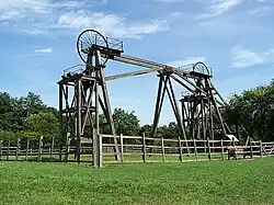 Twin timber frames of winding gear topped with spoked metal wheels used to hoist men and coal from underground on a sunny day