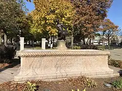 A large, rectangular, pink granite base with a smaller, aged bronze statue of a boy and turtle sitting in the center of the base.