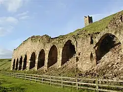 Ruinous stone arches set into a hillside, with a chimney on top