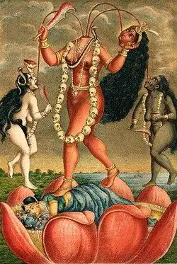 A decapitated, nude, red-complexioned goddess stands on a copulating couple inside a large lotus. She holds her severed head and a scimitar. Three streams of blood from her neck feed her head and two nude, red-coloured women holding a scimitar and a male severed head, who flank her. All three wear a garland of severed heads, a serpent (around her neck) and various gold and pearl jewellery.