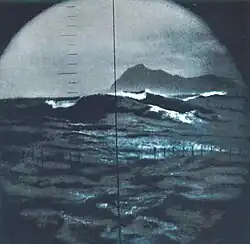 Capt Horn as seen from the periscope of the nuclear submarine USS Triton is a rugged, jagged-edge mountainous rock formation rising above heavy sea swells under a stormy sky.