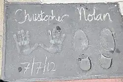 A hand and footprint reading "Christopher Nolan" at the top and "7/7/2012" at the bottom.