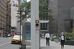 A pylon at the northeast corner of Lexington Avenue and 53rd Street. The pylon is square and painted gray. There are pedestrian traffic signals embedded into the sides of the pylon.