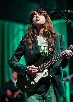 A young Caucasian woman in green clothing looking sideways while holding a guitar