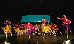 Collegiate Garba-Raas team on stage, captured during Raas section of performance (holding dandiyas) dressed in traditional attire