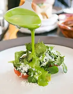 Some edible herbs with cheese served over tomatoes. A waiter covers them with a sauce.