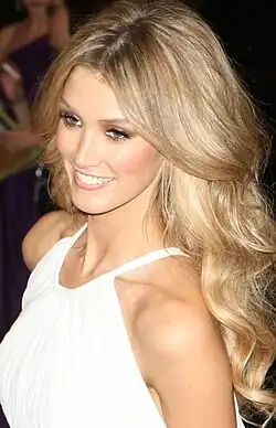 A blonde woman wearing a white dress smiles off into the distance
