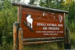 Wooden rectangular sign saying "Denali National Park and Preserve" with pictures of a mountain goat and a mountain