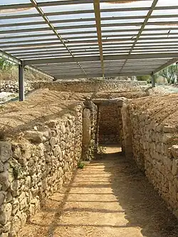 View down the passageway of an ancient tomb, made out of limestone blocks: the camera looks at a doorway into the burial chamber.