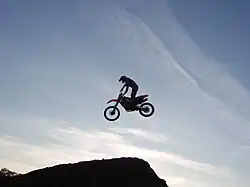 A silhouette of an airborne dirt bike rider against a sky with wispy clouds
