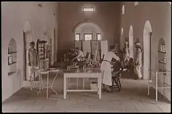 Sepia-toned photograph showing a room in a hospital with two seated patients being seen by medics.