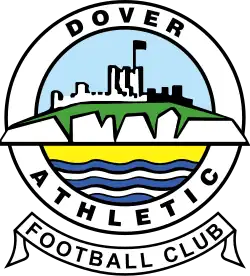 A simplified illustration of a castle atop white cliffs, with the sea below, all surrounded in a circular border containing the words "Dover Athletic", with a scroll below containing the words "Football Club"