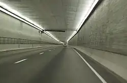 A two-lane freeway without any safety lanes or shoulders is proceeding down a lighted square passageway.