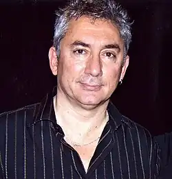 close-up of Erick Benzi wearing a black striped shirt, looking with a slight smile directly at camera