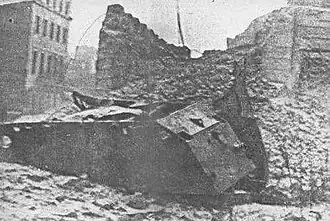 Wreck of a mine-vehicle on Kiliński Street in Warsaw among rubble and destroyed buildings
