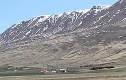 Farm and town buildings seen from a distance with mountains looming in the background