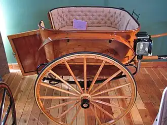 This image shows the rear door. This cart has button-tufted upholstery, carriage lamps, semi-elliptical springs, and rubber-clad wheels.