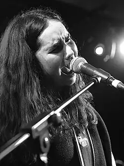 Black and white photograph of Francis of Delirium from the chest up, closely cropped. She is wearing a hoodie and singing intensely into a microphone on a stand with her head tilted and her eyes closed.
