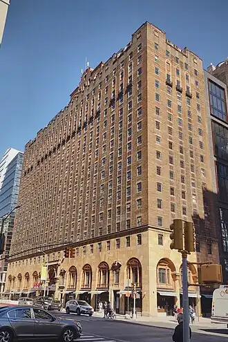 A tall rectilinear brown brick building on a city street corner with regularly spaced windows and arches along the street level