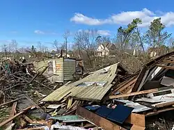 A destroyed and collapsed home in front of damaged trees