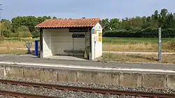 A small one room train stop with a red roof. It contains a single bench.