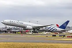 A wide, navy blue plane takes off of Sydney Airport. Qantas airplanes can be seen in the background.