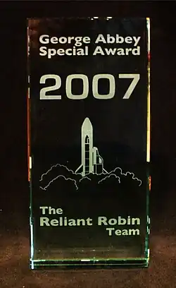 A 2007 George Abbey Award, stating in white text "George Abbey Special Award, 2007. The Reliant Robin Team." Depicted is a drawing of a rocket launching with a Reliant Robin attached to it.