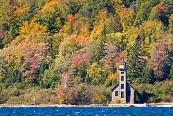 Small lighthouse standing on the lakeshore in front of trees in fall colors